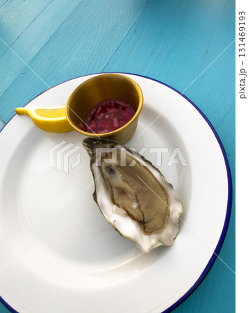 Plate with oyster, lemon slice, and condiment cup on blue surface Plate with oyster, lemon slice, and condiment cup on blue surface 131469193