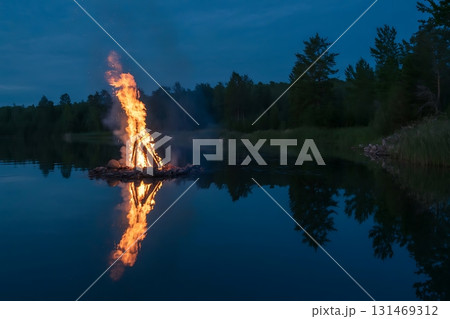 A bonfire burning brightly on a raft in the middle of a dark blue lake 131469312