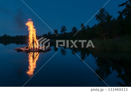 Bonfire burning on a raft in the middle of a lake at night with reflection 131469313