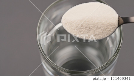 Close-up of a spoon with collagen or protein powder held over a glass of water. Concept of dietary supplement, healthy lifestyle, nutrition, beauty care and soluble wellness product preparation Close-up of a spoon with collagen or protein powder held over a glass of water. Concept of dietary supplement, healthy lifestyle, nutrition, beauty care and soluble wellness product preparation 131469341