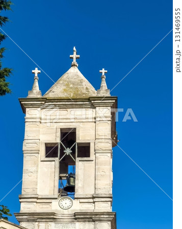An old bell tower with a clock against the background of a bright blue sky. 131469555