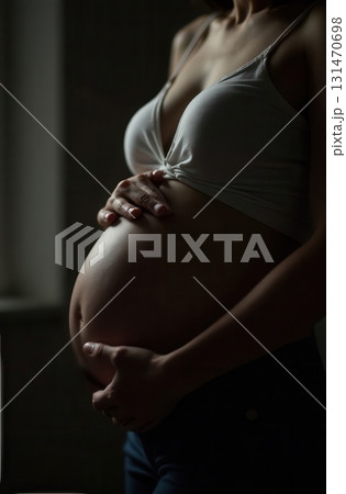 Pregnant woman holding her belly near a window in a dark room Pregnant woman holding her belly near a window in a dark room 131470698