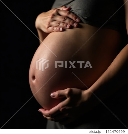 Pregnant woman holding her belly on black background 131470699