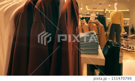 View of clothing racks, folded jeans, and mannequins inside a generic fashion retail store. Stylish contemporary interior with warm lighting and neatly arranged garments View of clothing racks, folded jeans, and mannequins inside a generic fashion retail store. Stylish contemporary interior with warm lighting and neatly arranged garments 131470799