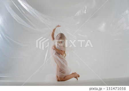 Elegant blonde woman poses gracefully in a studio with flowing fabric 131471038