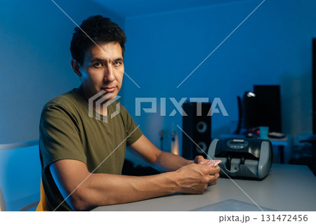 Young cashier preparing banknotes for electronic counting machine while working late in office with blue light, focusing on financial tasks and money management, looking at camera. 131472456