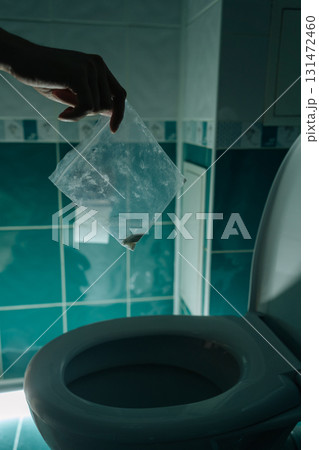Vertical cropped shot of male hand holding plastic bag with drugs over open toilet, ready to dispose of illegal substance in dark bathroom, representing drug abuse, disposal and dealing with addiction Vertical cropped shot of male hand holding plastic bag with drugs over open toilet, ready to dispose of illegal substance in dark bathroom, representing drug abuse, disposal and dealing with addiction 131472460