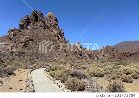 A rocky landscape with a winding path leading through dry vegetation in Roques de Garcia, volcano Teide National Park, Tenerife A rocky landscape with a winding path leading through dry vegetation in Roques de Garcia, volcano Teide National Park, Tenerife 131472784