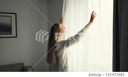 Woman opening window curtains at home in morning 131472981