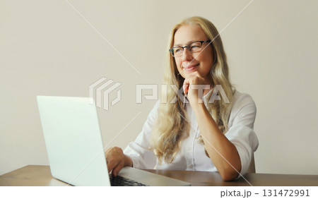 Happy woman working with laptop sitting at desk in office or at home Happy woman working with laptop sitting at desk in office or at home 131472991