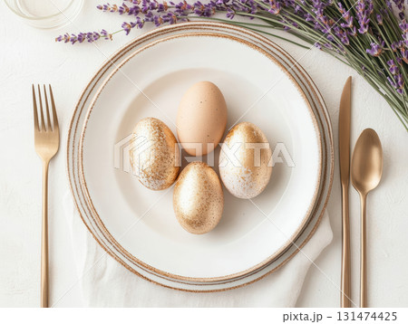 Happy Easter. Elegant top view, layout, minimalist style, Easter decorated table with golden eggs and lavender bouquet arranged on napkin with matching cutlery and glassware. 131474425