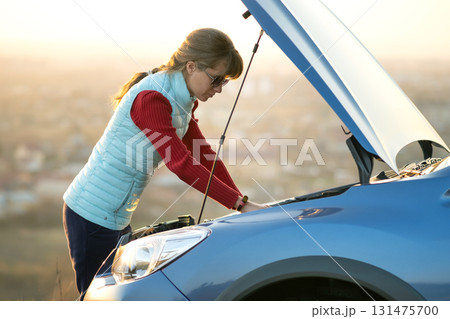Young woman standing near broken down car with popped up hood having trouble with her vehicle. Young woman standing near broken down car with popped up hood having trouble with her vehicle. 131475700