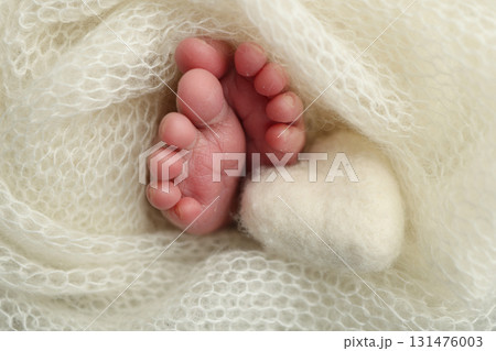 Soft feet of a new born in a white wool blanket. Close up of toes, heels and feet of a newborn. Knitted white heart in the legs of a baby. Macro photography.The tiny foot of a newborn baby 131476003
