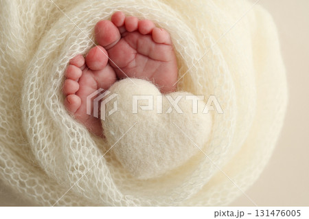 Soft feet of a new born in a white wool blanket. Close up of toes, heels and feet of a newborn. Knitted white heart in the legs of a baby. Macro photography.The tiny foot of a newborn baby 131476005