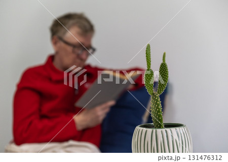 elderly person reading book with cactus plant in cozy indoor setting. selective focus. closeup. 131476312
