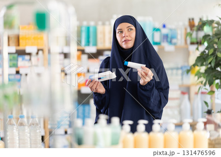 Young woman in hijab chooses ointment at pharmacy Young woman in hijab chooses ointment at pharmacy 131476596