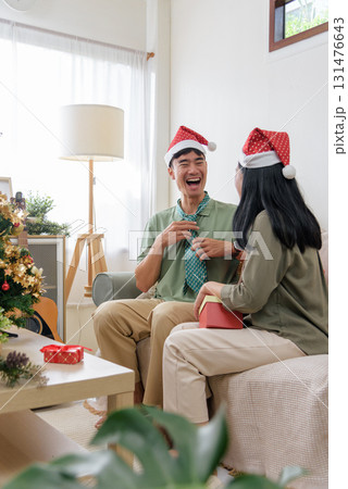 Christmas happy couple shares love, enjoying winter holiday at home, laughing joyfully, wearing festive santa hats, exchanging gifts during cozy christmas celebration. 131476643