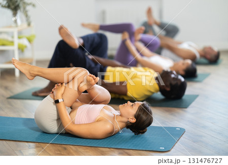 Woman performing Reclining pigeon pose with group in yoga studio 131476727