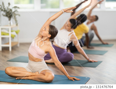 Young woman coach and students perform variation of lotus asana during training in studio 131476764