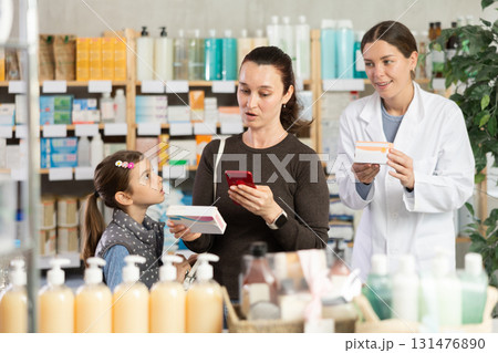 Woman checking vitamins info online for preteen daughter at pharmacy 131476890