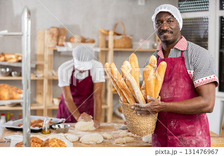 African male cook-baker worker with basket of baguettes, shows many products African male cook-baker worker with basket of baguettes, shows many products 131476967