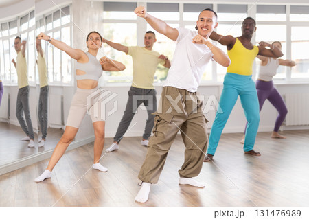 Young Asian male instructor guiding group through zumba routine Young Asian male instructor guiding group through zumba routine 131476989