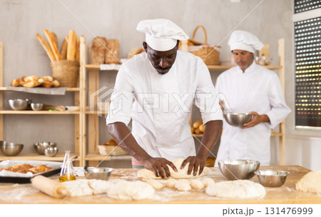 African man works as baker in bakery, molds pies from dough, creates croissants from dough 131476999