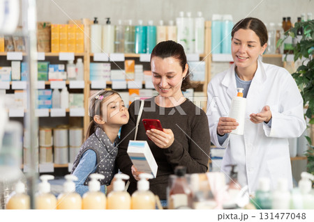 woman with her daughter scans a mobile package of cream in a pharmacy woman with her daughter scans a mobile package of cream in a pharmacy 131477048
