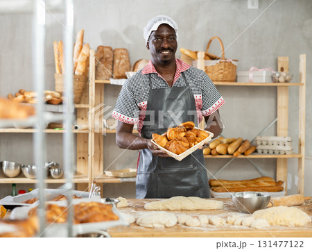 Happy male chef showing off croissants in his bakery Happy male chef showing off croissants in his bakery 131477122
