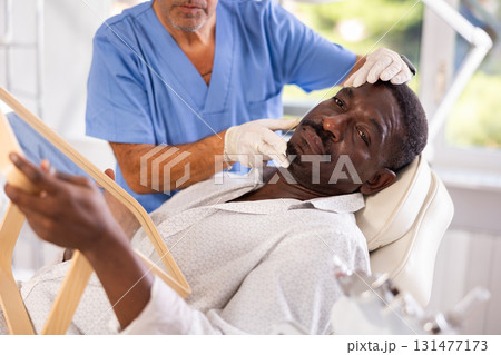 Male cosmetologist examines face of African man patient and consult on possibility of rejuvenation 131477173