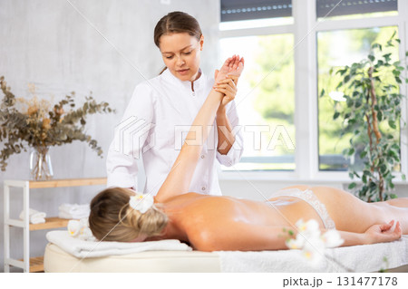During massage, female physiotherapist stretch girl client arm to improve mobility of shoulder joint 131477178