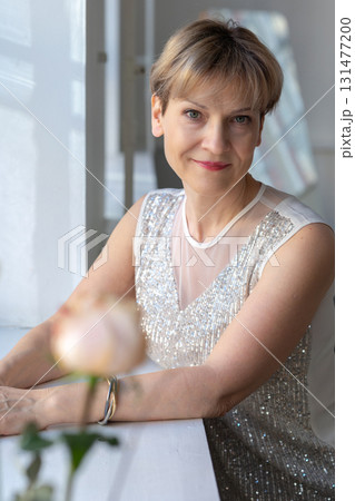 Portrait of smiling woman in festive clothes against a gray wall in a bright sunny room. Vertical photo. High quality photo 131477200