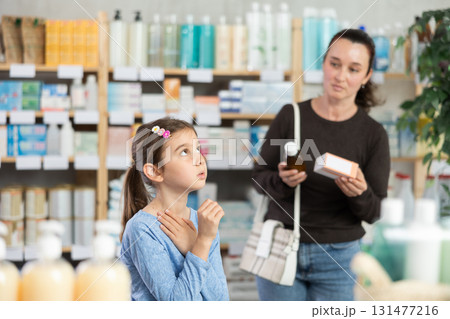 child stands and coughs in the pharmacy, and the mother chooses medications child stands and coughs in the pharmacy, and the mother chooses medications 131477216