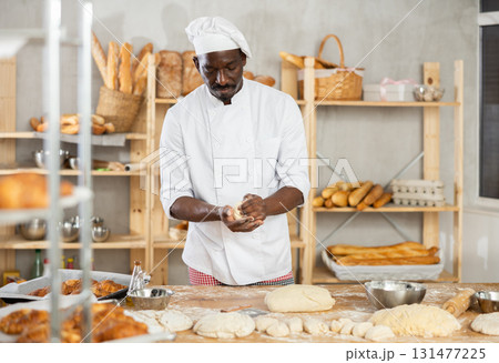 African baker forming dough pieces on floured table in bakery African baker forming dough pieces on floured table in bakery 131477225