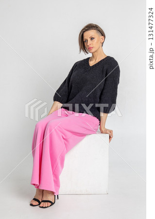 Portrait beautiful woman of model appearance. Girl in black jumper and pink trousers on grey background. Pretty female with trendy makeup posing in studio. Vertical photo.  131477324