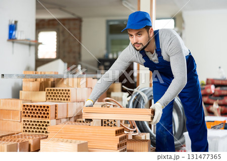Young contractor stacking bricks on construction site indoors Young contractor stacking bricks on construction site indoors 131477365
