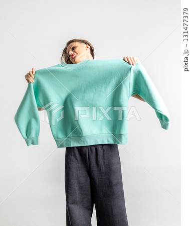 Portrait beautiful woman of model appearance. Girl in mint jumper, black trousers on grey background. Pretty female with trendy makeup posing in studio. Vertical photo. Portrait beautiful woman of model appearance. Girl in mint jumper, black trousers on grey background. Pretty female with trendy makeup posing in studio. Vertical photo. 131477379