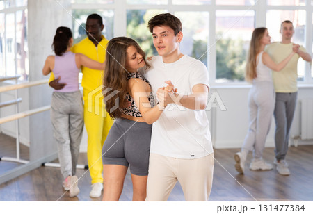 Smiling young couple enthusiastically dancing social latin cha-cha-cha dance in dance salon Smiling young couple enthusiastically dancing social latin cha-cha-cha dance in dance salon 131477384