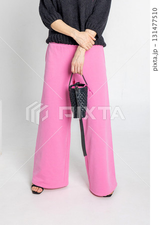 Portrait beautiful woman of model appearance. Girl in black jumper and pink trousers on grey background. Pretty female with trendy makeup posing in studio. Vertical photo.  131477510