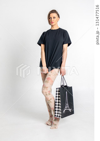 Woman in light tights and black T-shirt with black gift bag in French style on light background. Vertical photo. High quality photo 131477516