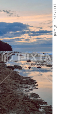 Peaceful scene of ice floes drifting in calm ocean waters with stunning sunset sky. Reflective water surface captures colorful clouds, evoking serenity and tranquility. Vertical photo Peaceful scene of ice floes drifting in calm ocean waters with stunning sunset sky. Reflective water surface captures colorful clouds, evoking serenity and tranquility. Vertical photo 131477531