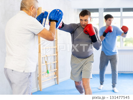 Man in boxing gloves practicing punches on mitts during self-defense course 131477545