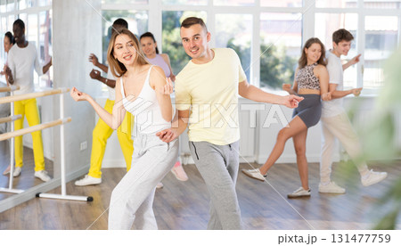 Happy young woman and man with group of multinational people enjoying active boogie-woogie dance in studio Happy young woman and man with group of multinational people enjoying active boogie-woogie dance in studio 131477759