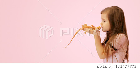 Portrait of pretty girl with Red bearded Agama iguana on pink background. Little child playing with reptile. Selective focus. Banner, copy space. High quality photo 131477773