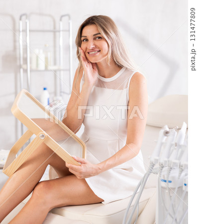 Young joyful woman examining her face after cosmetic procedure Young joyful woman examining her face after cosmetic procedure 131477809