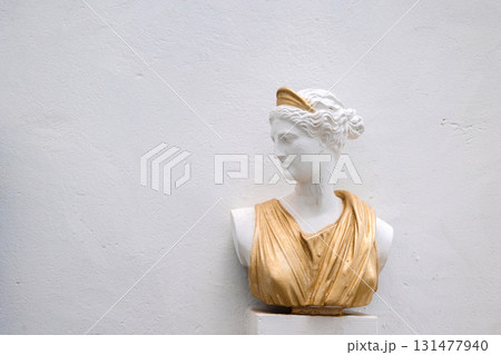 Antique head bust of woman against gray wall. Historical statue in golden dress himation. Ancient female face on light background. High quality photo Antique head bust of woman against gray wall. Historical statue in golden dress himation. Ancient female face on light background. High quality photo 131477940
