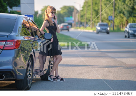 Stylish woman driver standing near her vehicle talking on cellphone on city street in summer 131478467