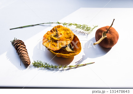 Dried pumpkin - container with a lid and a dried mandarin with a leaf, horsetail, and a spruce cone on a white background. Still life. Dried pumpkin - container with a lid and a dried mandarin with a leaf, horsetail, and a spruce cone on a white background. Still life. 131478643