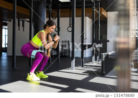 Fitness woman making squat with rubber band training butts at sportive gym 131478680
