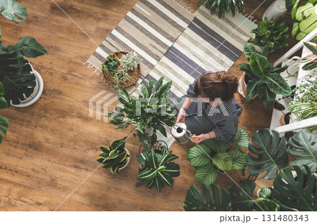 A young woman enjoys caring for flowers. Watering indoor plants and admiring them. 131480343